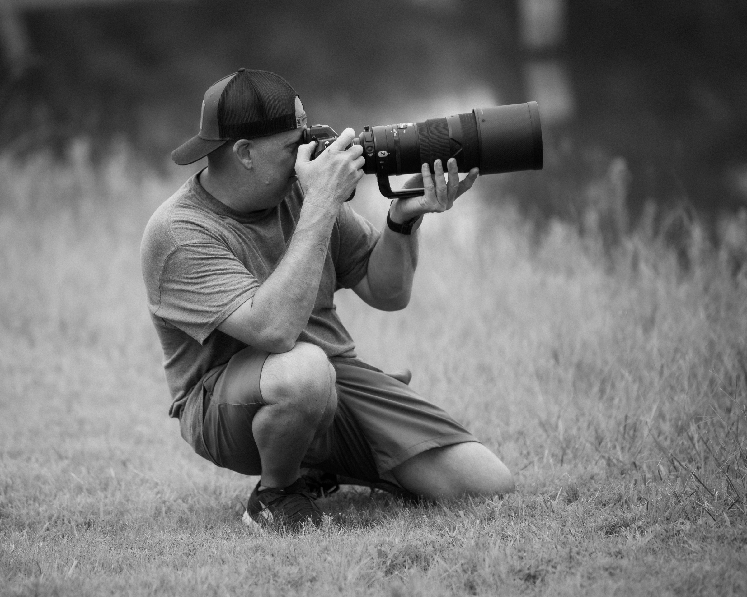 Chris Davis of Davis Dog Sports Media, kneeling in the field with a long telephoto lens